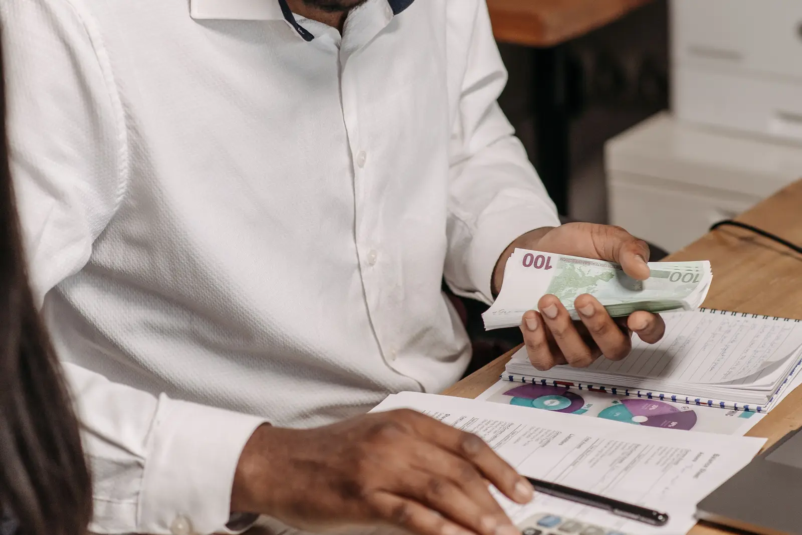 Commerçant comptant des billets de 100 euros à son bureau, carnet et documents comptables ouverts devant lui