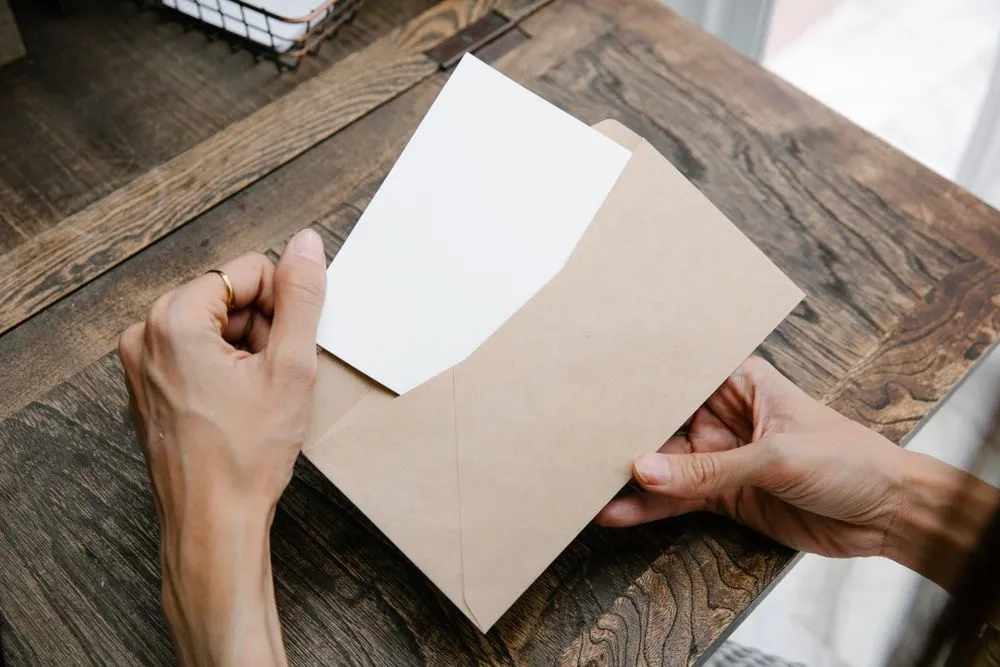 Mains ouvrant une enveloppe contenant un courrier sur un bureau en bois