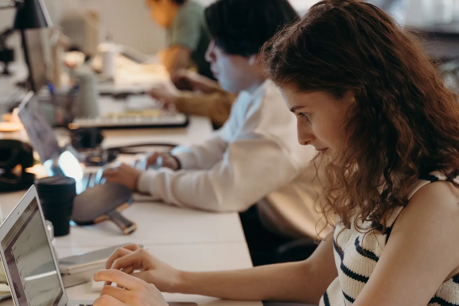 Femme concentrée devant son ordinateur portable dans un bureau partagé, collègues au travail en arrière-plan