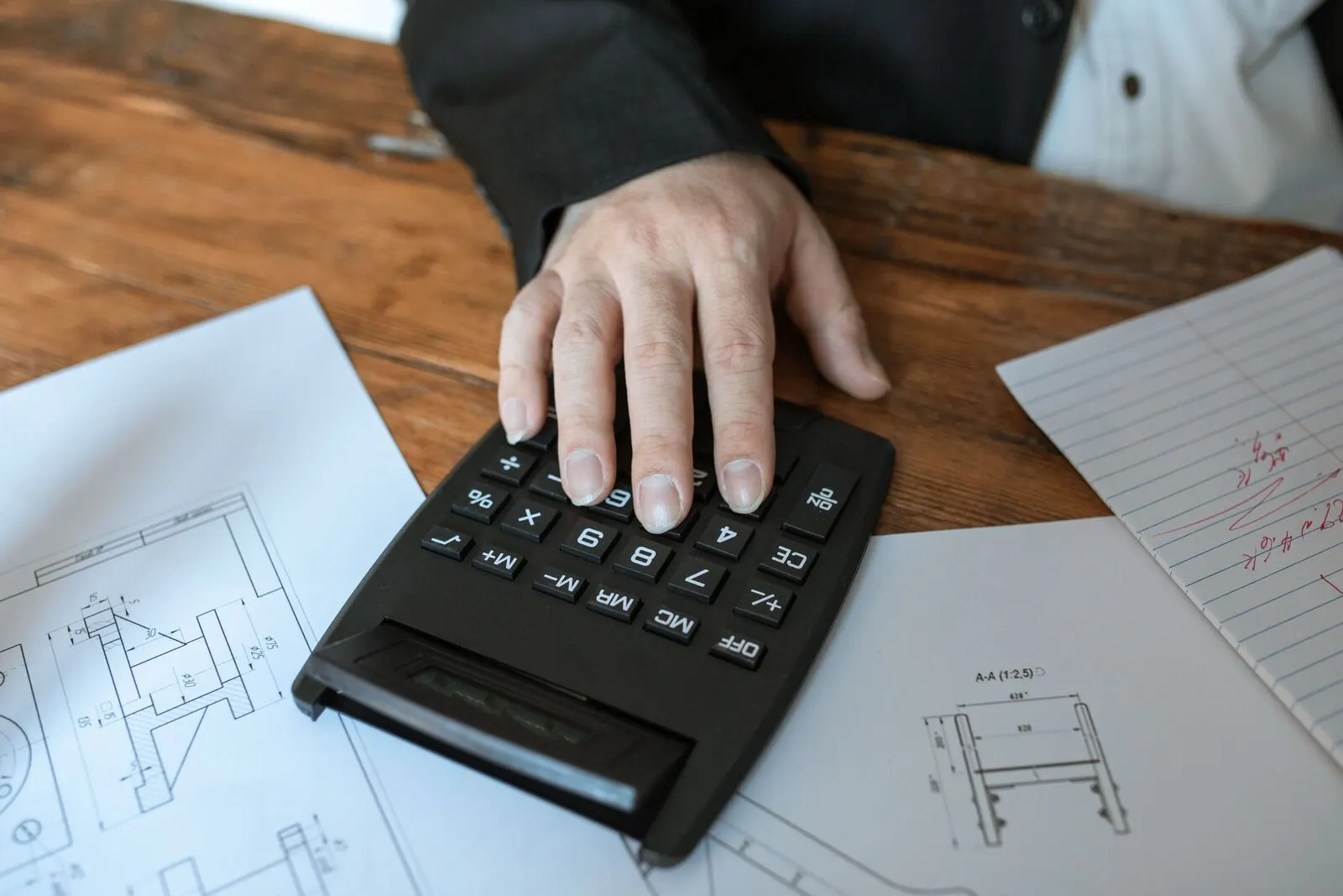 Main sur une calculatrice au milieu de documents techniques, pour comparer des tarifs de plateformes agréées